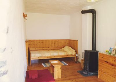 Doppelzimmer im Dharmahaus mit Bett, Ofen und Meditationsplatz