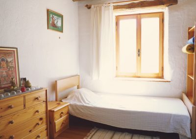 Einzelzimmer im Dharmahaus mit Bett, Ofen und Meditationsplatz